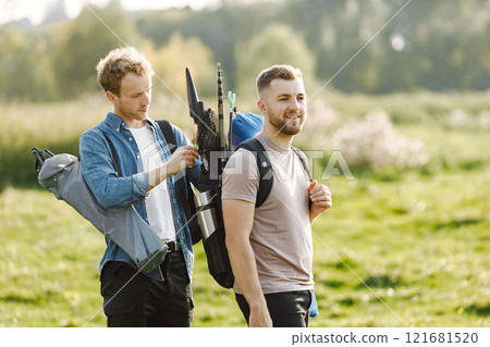 Friends is ready to fishing. Man holding a fishing equipment and other helps him. One man wearing rose t-shirt and other blue shirt. Friends is ready to fishing. Man holding a fishing equipment and other helps him. One man wearing rose t-shirt and other blue shirt. 121681520