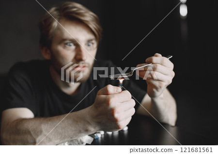 Junkie man sitting in dark room and heating spoon with heroin on lighter. Junkie man sitting in dark room and heating spoon with heroin on lighter. 121681561