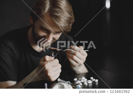 Junkie man sitting in dark room and heating spoon with heroin on lighter. 121681562