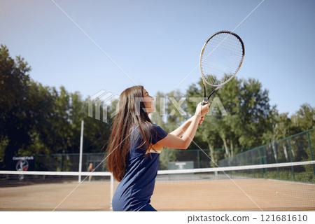 Tennis player woman focused during play. Caucasian woman playing tennis on the court outdoors. Woman wearing blue sport dress. Tennis player woman focused during play. Caucasian woman playing tennis on the court outdoors. Woman wearing blue sport dress. 121681610