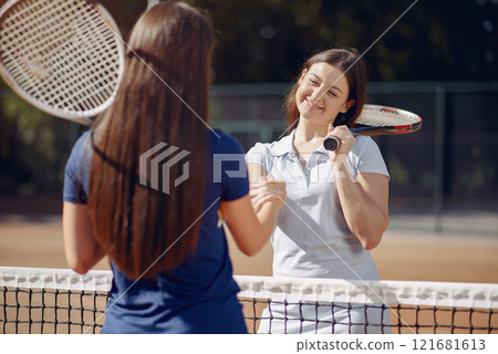 Image of two women shaking their hands while playing tennis on tennis court outdoors. Shot of a two young tennis players shaking hands over the net. Woman holding a racket. 121681613
