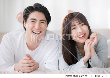 一對微笑的夫婦看著鏡頭,在臥室的床上放鬆地趴著 一對微笑的夫婦看著鏡頭,在臥室的床上放鬆地趴著 121681795
