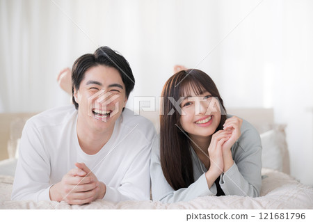 一對微笑的夫婦看著鏡頭，在臥室的床上放鬆地趴著 121681796