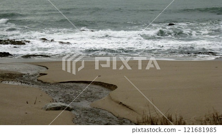 A coast with waves crashing and a river flowing into the sea 121681985