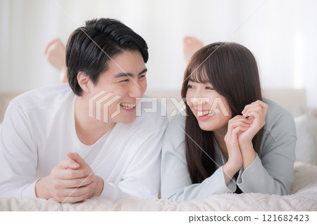 一對微笑的夫婦躺在臥室的床上,互相看著對方放鬆 一對微笑的夫婦躺在臥室的床上,互相看著對方放鬆 121682423