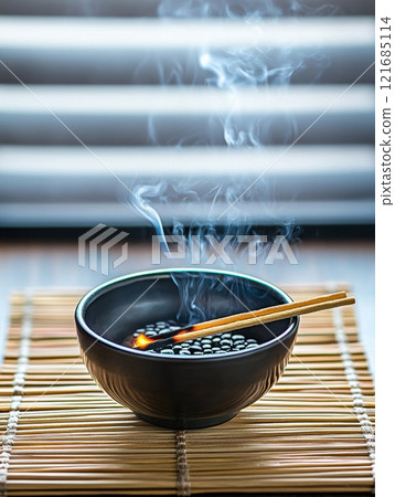 Smoke rising from a bowl of black beans with chopsticks resting on a bamboo mat in a calm setting Smoke rising from a bowl of black beans with chopsticks resting on a bamboo mat in a calm setting 121685114
