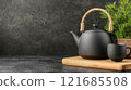 Black teapot and cup on wooden board with pine branches in a cozy indoor setting 121685508