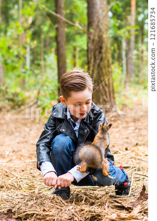 In the summer in the forest the boy feeds the squirrel with nuts 121685734