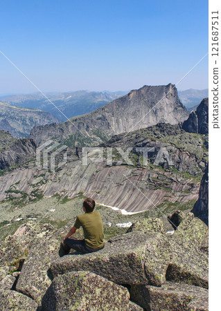 Man tourist sits on rock high in mountains. Panoramic view of mountain range Man tourist sits on rock high in mountains. Panoramic view of mountain range 121687511