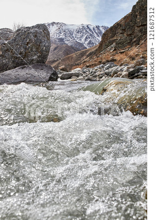 Boiling water splashes in mountain river against the backdrop of hills with snow 121687512