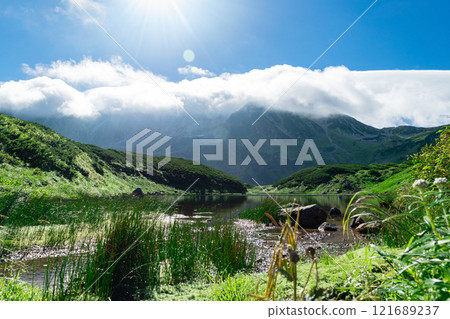 A mountainous area with blue sky, clouds, mountains and a lake 121689237
