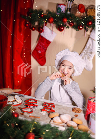 Cheerful girl in chef's hat eating homemade cookies on Christmas background 121689779