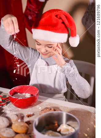 Joyful girl in Santa hat baking cookies during Christmas holiday celebrations 121689796
