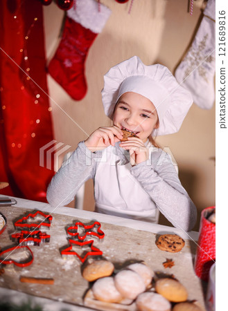Smiling child in a chef hat enjoying cookies in a festive kitchen setting 121689816