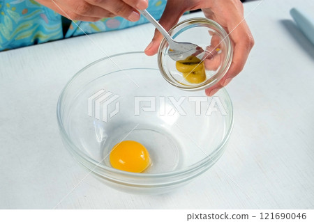 Woman cooking homemade mayonnaise adding mustard in bowl to yolk at home. Woman cooking homemade mayonnaise adding mustard in bowl to yolk at home. 121690046