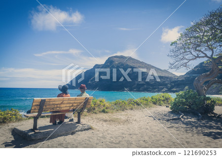 Elderly couple looking out at the ocean from a beach bench on the east coast of Hawaii 121690253