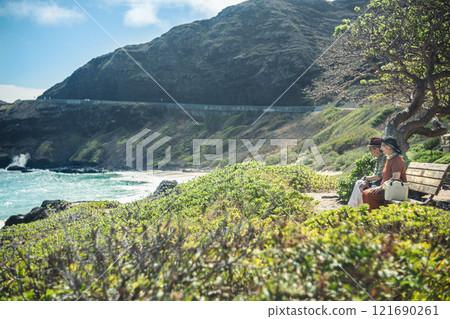 Elderly couple looking out at the ocean from a beach bench on the east coast of Hawaii 121690261