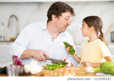 Happy father and daughter share a moment of joy in family kitchen, preparing vegetable salad 121690281