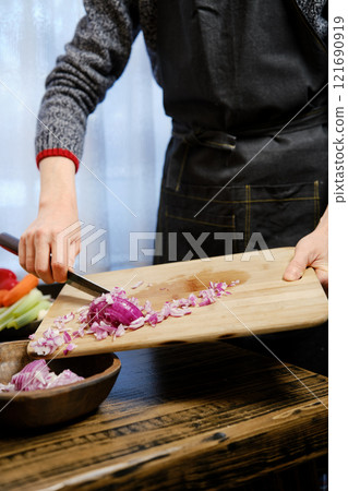 Unrecognizable man puts chopped red onions from a wooden cutting board in wooden bowl 121690919