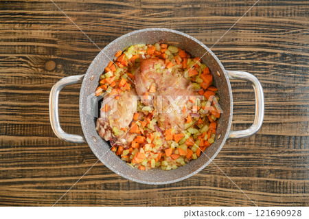 Cooking turkey thighs with diced vegetables in a metallic pot on a wooden countertop Cooking turkey thighs with diced vegetables in a metallic pot on a wooden countertop 121690928