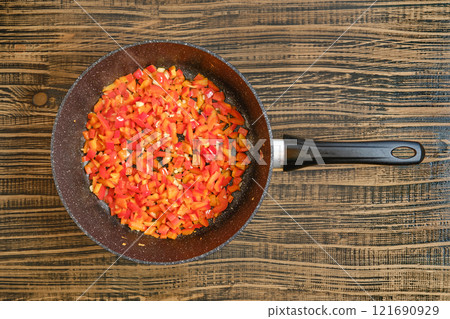 Chopped colorful bell peppers sauteing in a frying pan on a rustic wooden surface Chopped colorful bell peppers sauteing in a frying pan on a rustic wooden surface 121690929