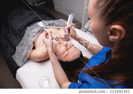 Happy woman gets ultrasonic facial massage with ultrasonic facial machine. Woman undergoing electric facelift procedure in luxury beauty salon Happy woman gets ultrasonic facial massage with ultrasonic facial machine. Woman undergoing electric facelift procedure in luxury beauty salon 121692361