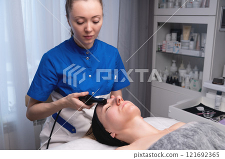 Woman undergoing skin tightening by activating a natural process. A cosmetologist performs a skin rejuvenation procedure in a spa. Aesthetic medical cosmetology Woman undergoing skin tightening by activating a natural process. A cosmetologist performs a skin rejuvenation procedure in a spa. Aesthetic medical cosmetology 121692365
