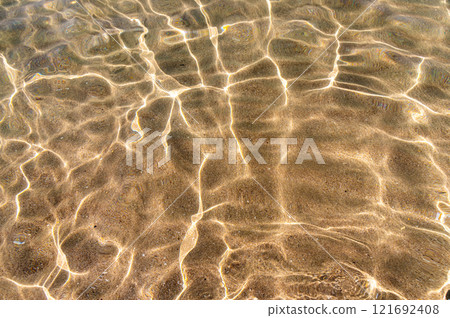 Through the transparent water of the ocean or sea you can see the sandy bottom with ridges of sand. Sun glare and ripples. View from above 121692408
