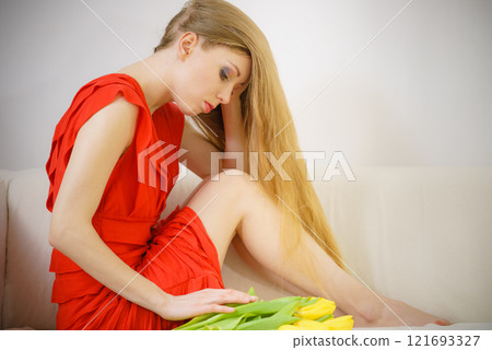 Sad elegant woman sitting on sofa with tulip 121693327