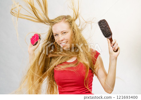 Blonde girl long blowing hair holds two brushes 121693400
