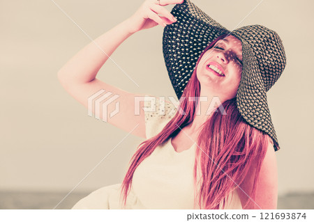 Redhaired happy girl in black hat on beach. 121693874