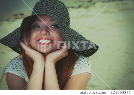 Redhaired happy girl in black hat on beach. Redhaired happy girl in black hat on beach. 121693875