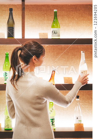 A young woman choosing Japanese sake [Photo courtesy of Niigata Jizake Premium SAKE Kura KURA] 121694205
