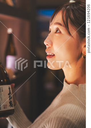A young woman choosing Japanese sake [Photo courtesy of Niigata Jizake Premium SAKE Kura KURA] 121694206