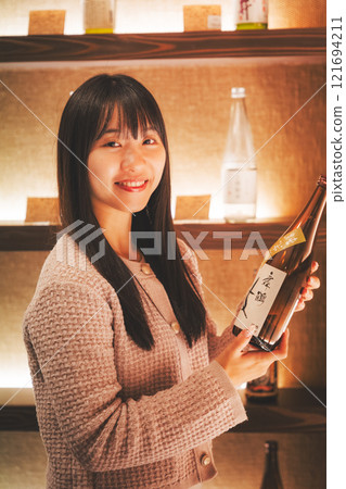 A young woman choosing Japanese sake [Photo courtesy of Niigata Jizake Premium SAKE Kura KURA] 121694211
