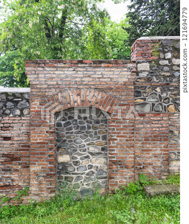Historic stone and brick wall with arched niche in a green setting Historic stone and brick wall with arched niche in a green setting 121694779