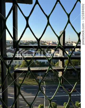 Cityscape View Through a Woven Metal Fence at Sunset 121694892