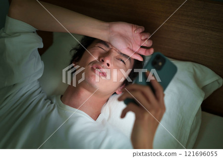 Middle-aged man lying down with smartphone Middle-aged man lying down with smartphone 121696055