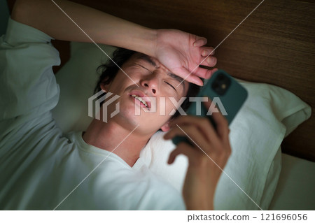 Middle-aged man lying down with smartphone Middle-aged man lying down with smartphone 121696056
