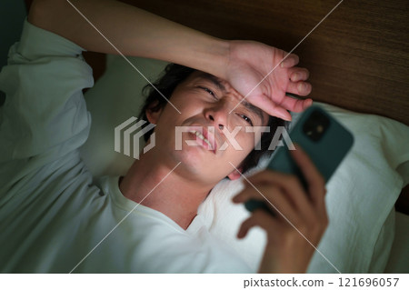 Middle-aged man lying down with smartphone Middle-aged man lying down with smartphone 121696057