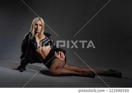 Stylish woman in a black leather jacket posing elegantly in a dark space Stylish woman in a black leather jacket posing elegantly in a dark space 121698589