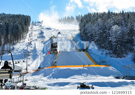 Preparing a ski slope for skiing, people are going up on a ski lift nearby. Preparing a ski slope for skiing, people are going up on a ski lift nearby. 121699315