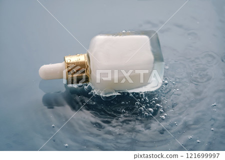 Bottle with white moisturizing serum in water on blue background. Bottle with white moisturizing serum in water on blue background. 121699997