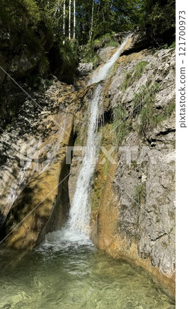 Scenic Waterfall Cascading Over Rocky Cliff Surrounded by Lush Green Trees in Berchtesgaden, Germany 121700973