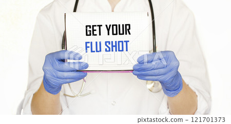 A doctor in blue medical gloves holds a notebook with the inscription GET a flu shot A doctor in blue medical gloves holds a notebook with the inscription GET a flu shot 121701373