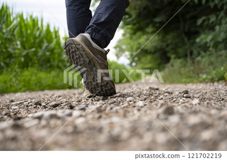 Low angle view of male feet in hiking shoes walking on a gravel path through green nature 121702219