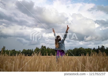 Joyful victorious young woman celebrating life as she stands with her arms raised high towards a dramatic cloudy sky 121702237