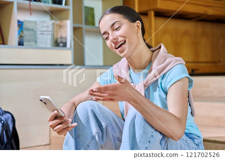 Teenage female student using smartphone, inside high school library 121702526