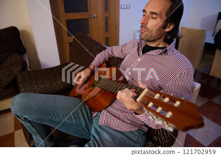 Man relaxing with acoustic guitar in a cozy living room setting Man relaxing with acoustic guitar in a cozy living room setting 121702959
