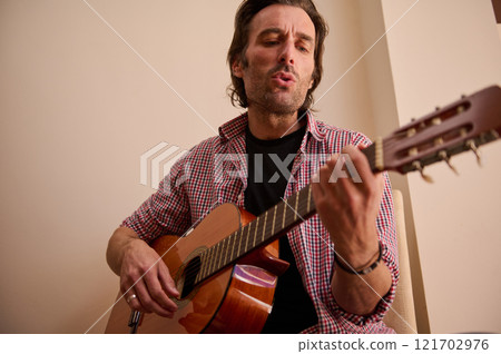 Man serenely playing a classical guitar and singing indoors Man serenely playing a classical guitar and singing indoors 121702976